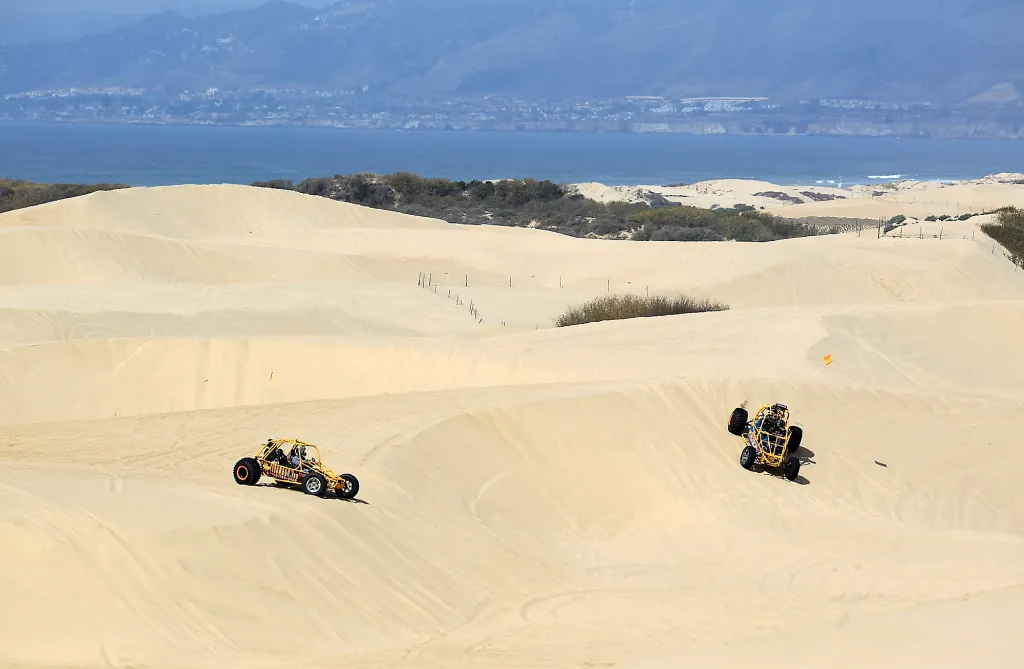 Two off-road vehicles drive on the sand dunes at Oceano Dunes State Vehicular Recreation Area.
