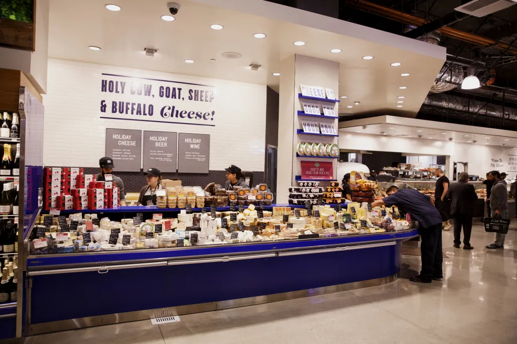 Various cheeses are displayed for sale in the specialty foods section of a Whole Foods Market.