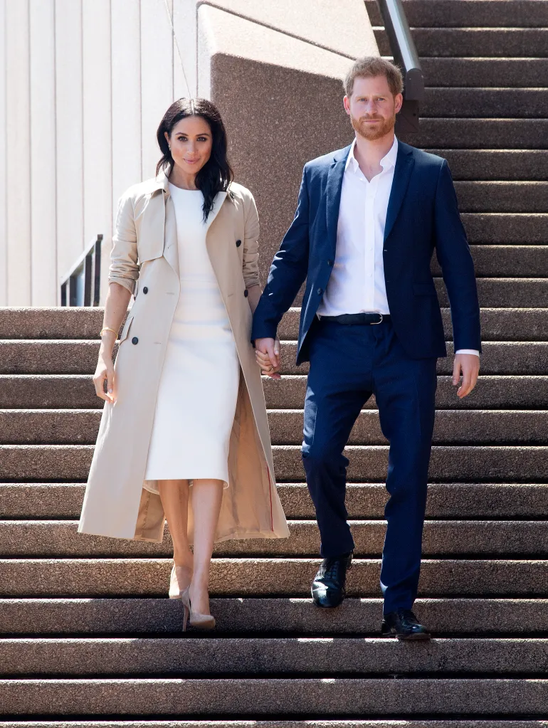 Prince Harry and Meghan Markle holding hands while walking down outdoor stairs.