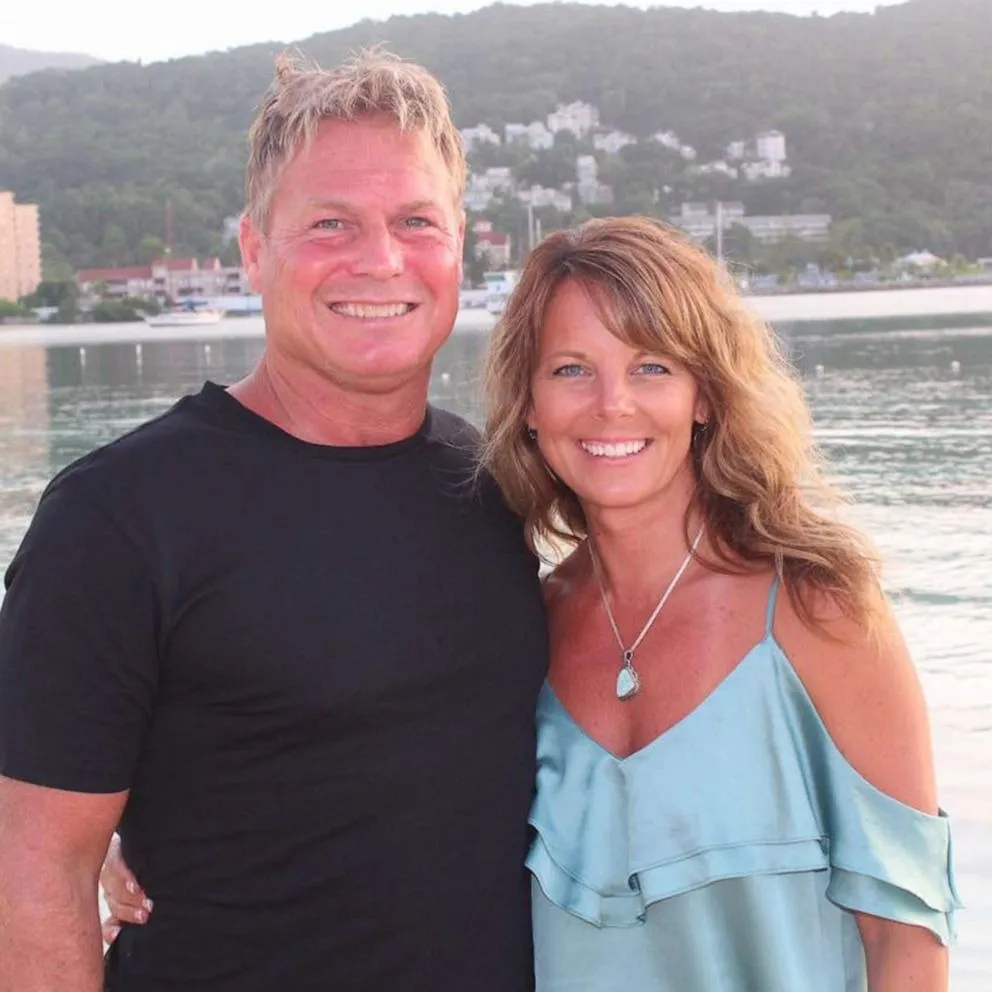 Barry and Suzanne Morphew smiling together with a body of water and hills in the background.