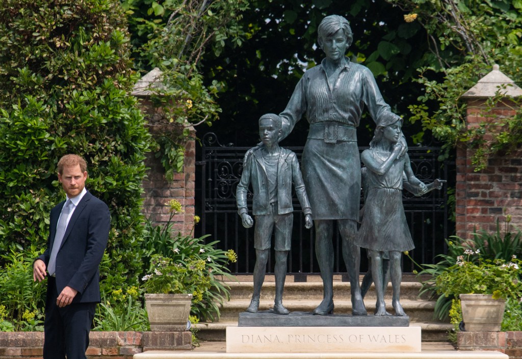 Prince Harry stands next to a statue of Princess Diana and three children in the Sunken Garden at Kensington Palace.