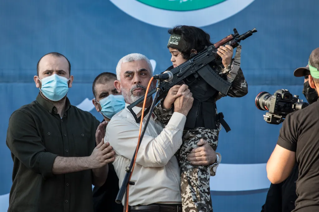 Yahya Sinwar holding a child in camouflage with a rifle at a ceremony for fighters.