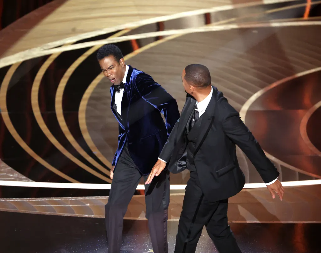 Chris Rock in a blue velvet tuxedo and Will Smith in a black tuxedo on stage.