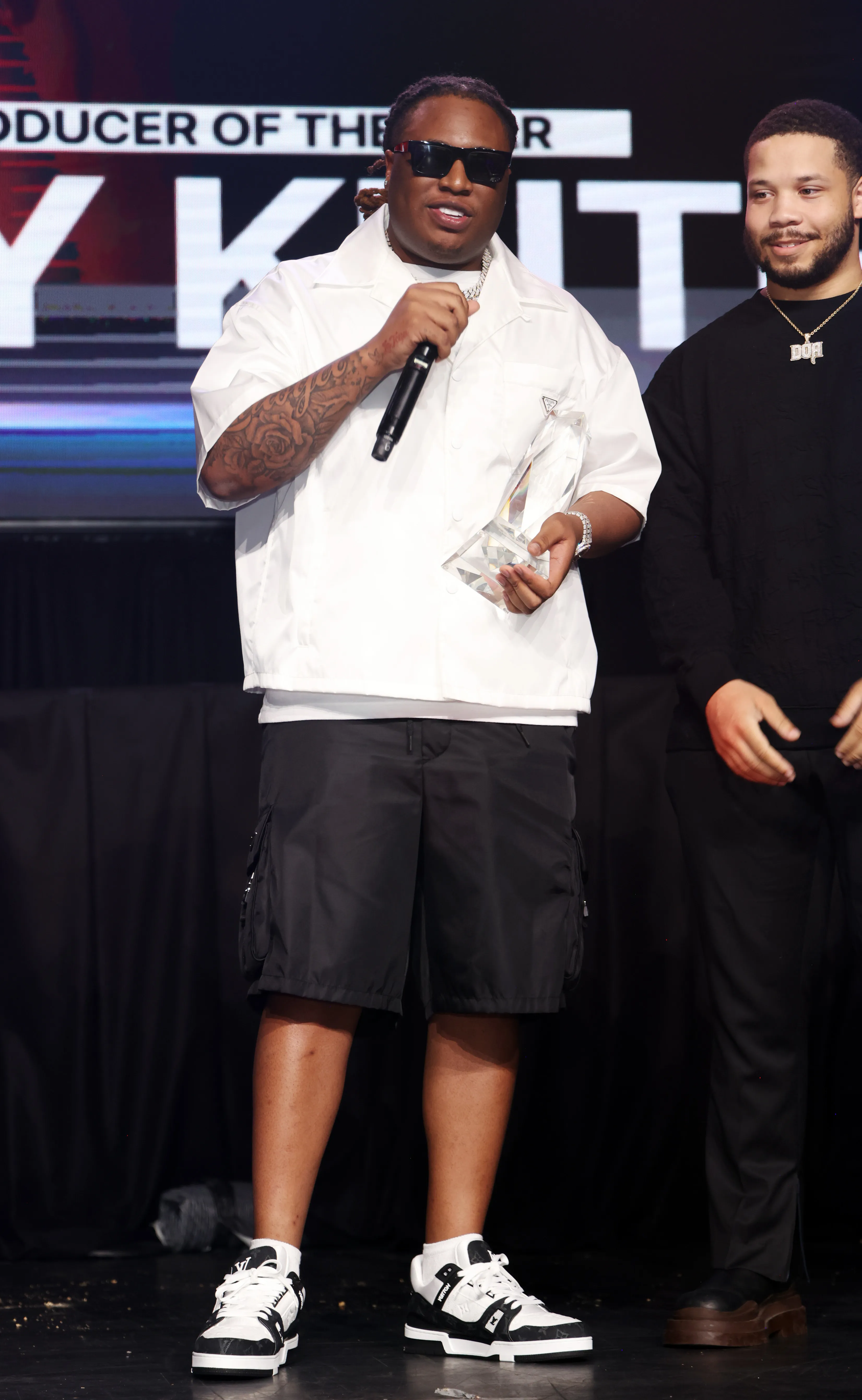 Tay Keith holding a clear award while speaking into a microphone.