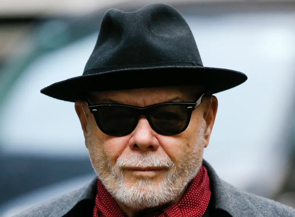Pop star Gary Glitter, whose real name is Paul Gadd, wearing a black hat, sunglasses, and a red polka dot scarf.