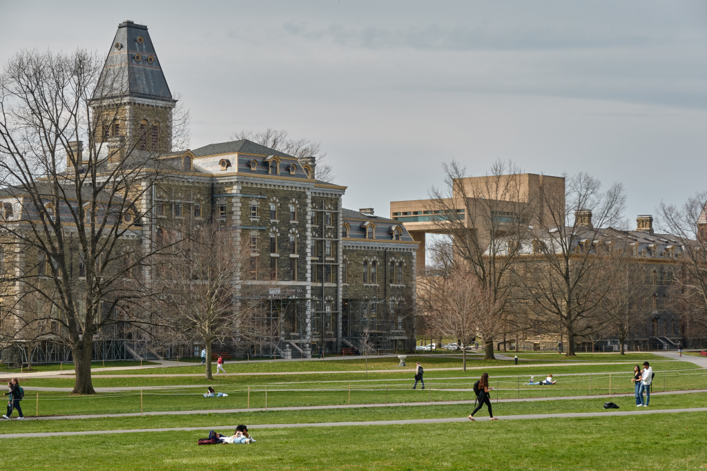 Students relaxing and walking on a grassy quad on the Cornell University campus.