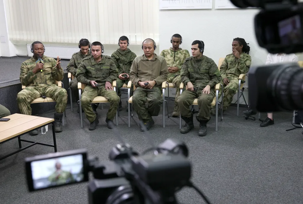 Captured foreign soldiers from Cuba, Nepal, Sierra Leone, and Somalia, wearing military fatigues and headphones, attend a press conference in Kyiv.