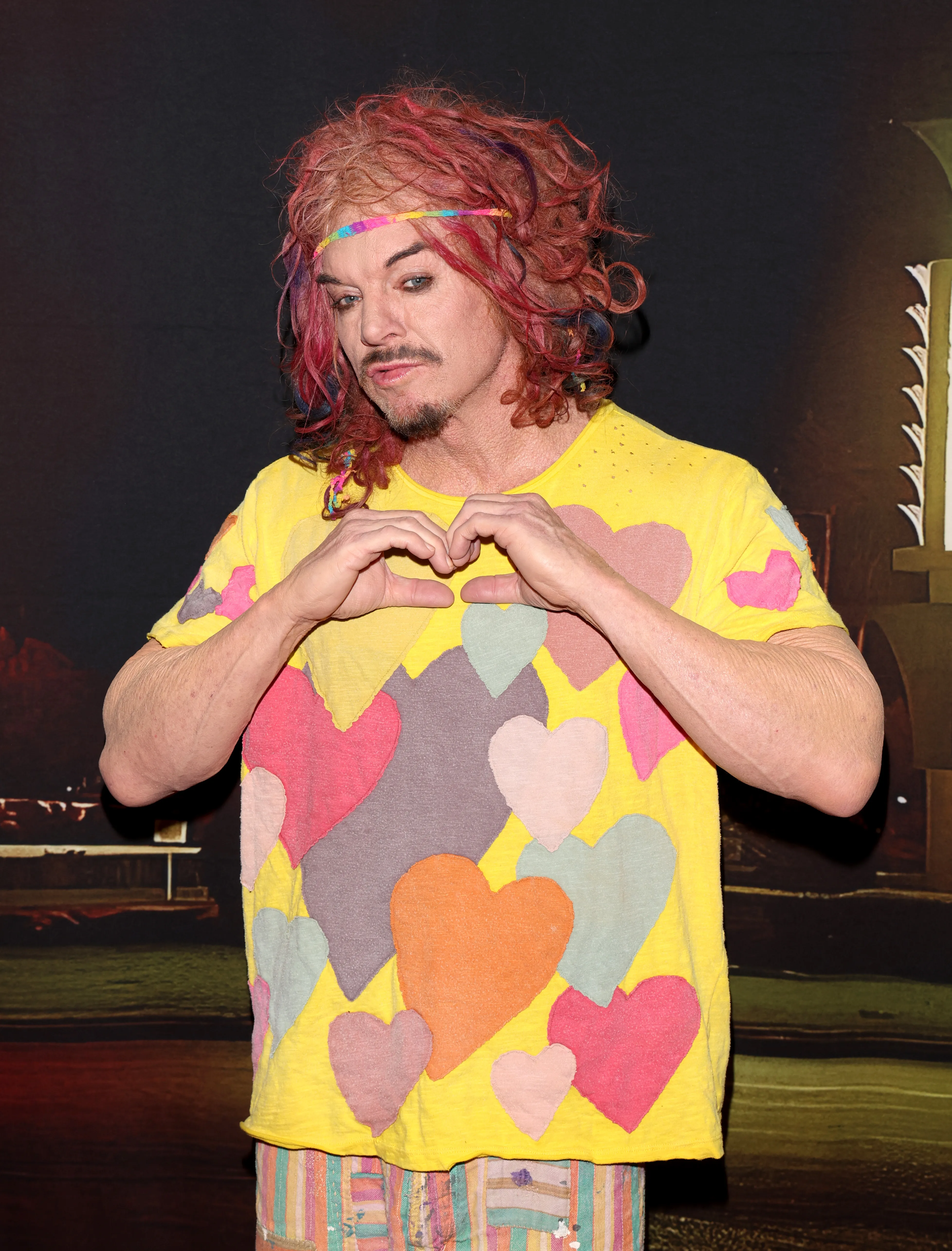 Carrot Top in a yellow shirt with colorful hearts making a heart shape with his hands.