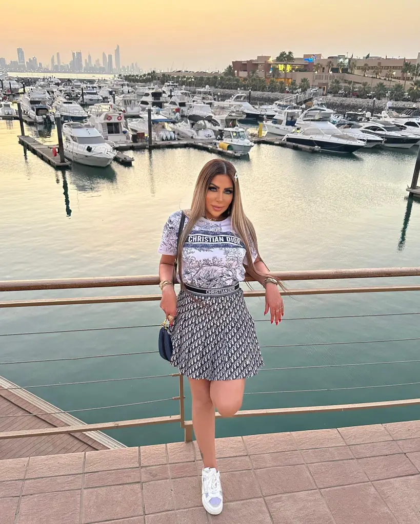 Sarah Khalifa in a white Christian Dior t-shirt and patterned skirt standing in front of a marina with boats.