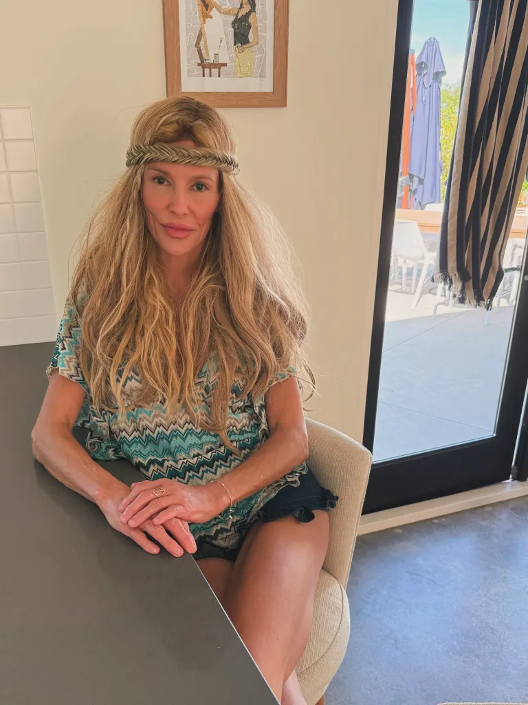 Brandi Glanville wearing a headband and patterned top, seated at a table.
