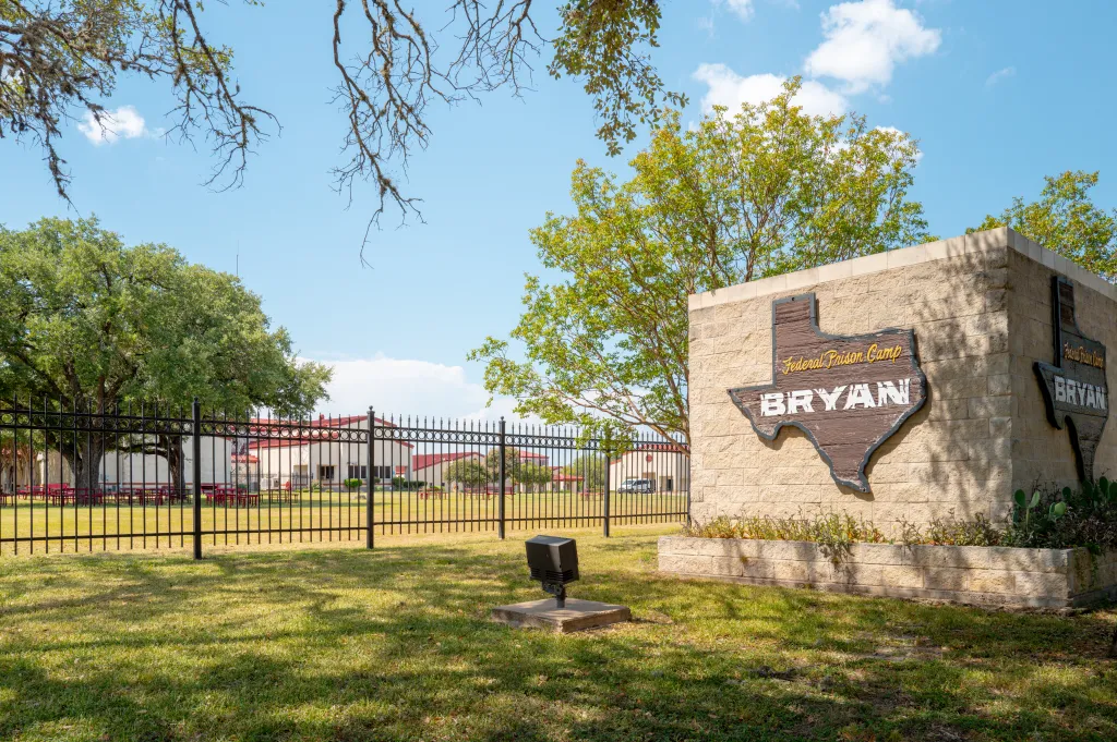 Signage for Federal Prison Camp Bryan, with buildings visible behind a fence.