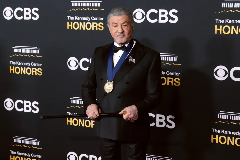 Sylvester Stallone posing at the Kennedy Center Honors with a cane and a medallion.