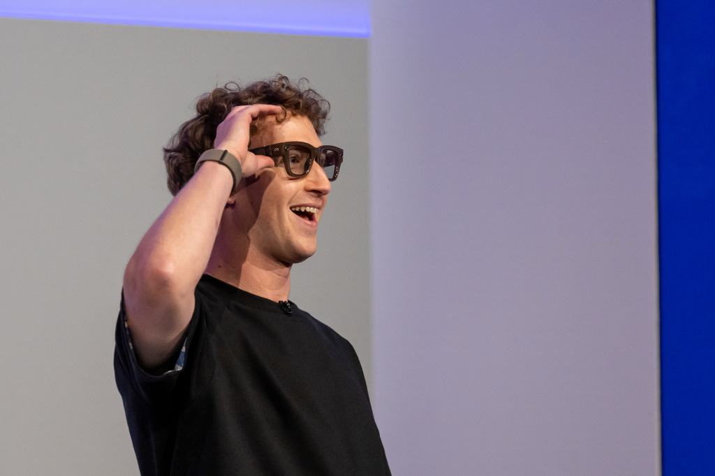 Mark Zuckerberg wearing Meta Ray-Ban Display AI glasses, with his hand on his head, smiling.