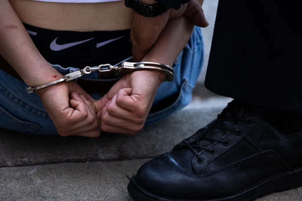 A protester in handcuffs is detained during an anti-ICE protest.