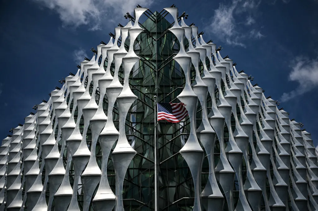 The American flag flies in front of a modern glass and steel building.