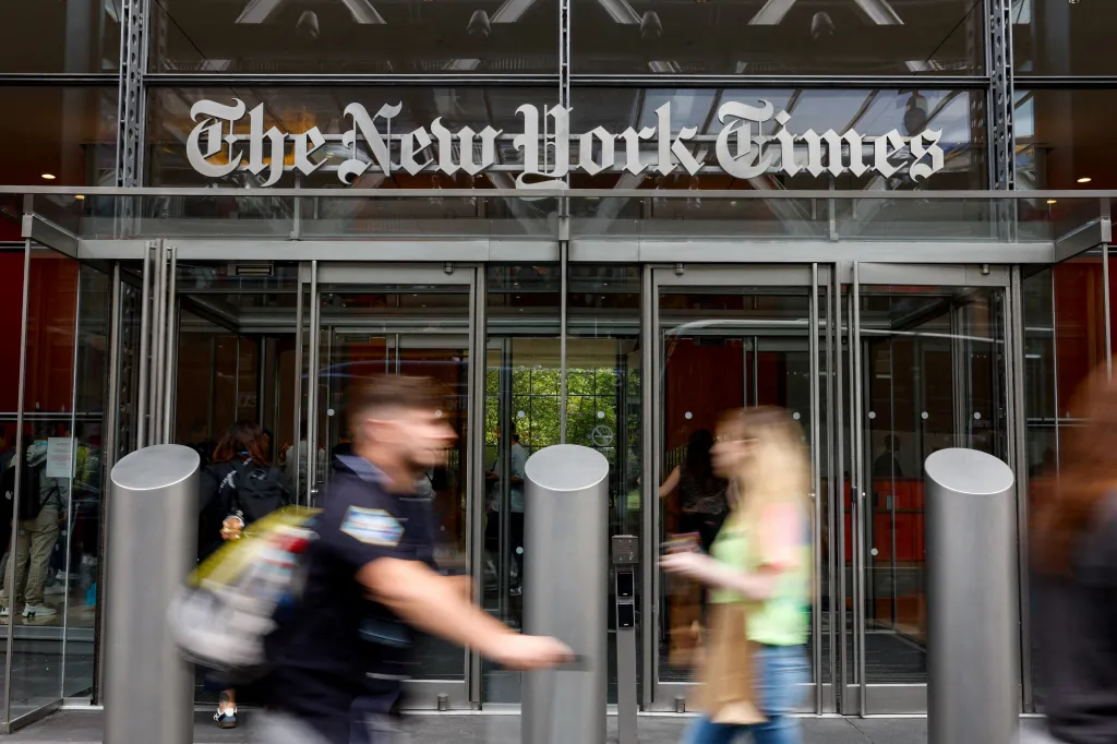The New York Times building with people walking in front of its glass entrance.