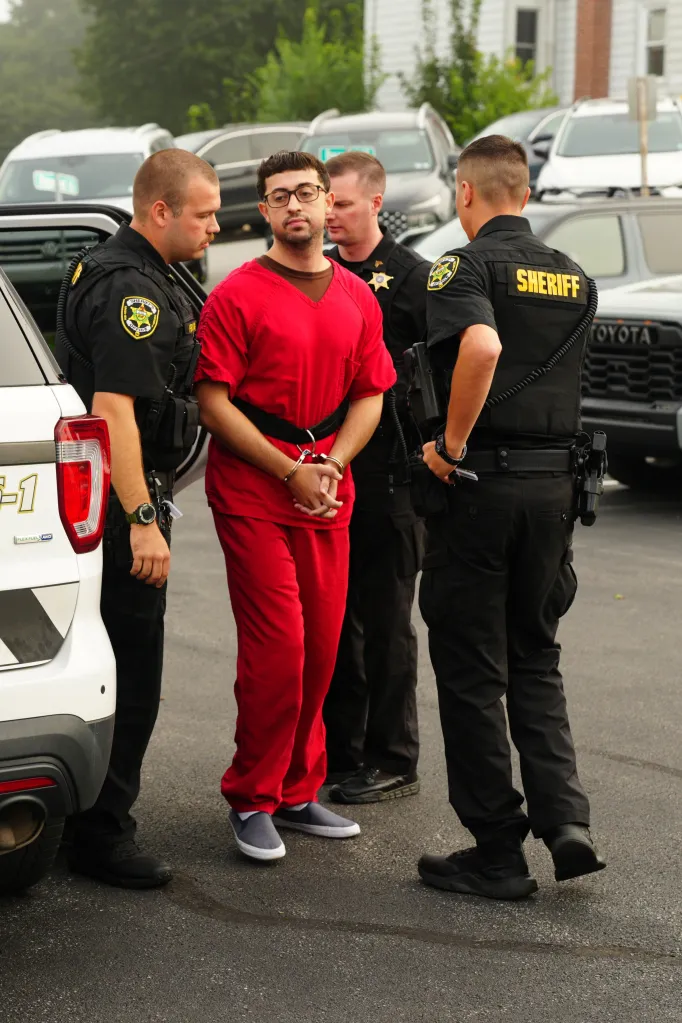 Agostino S. Abbatiello, handcuffed and wearing a red jumpsuit, escorted by two sheriff's deputies.