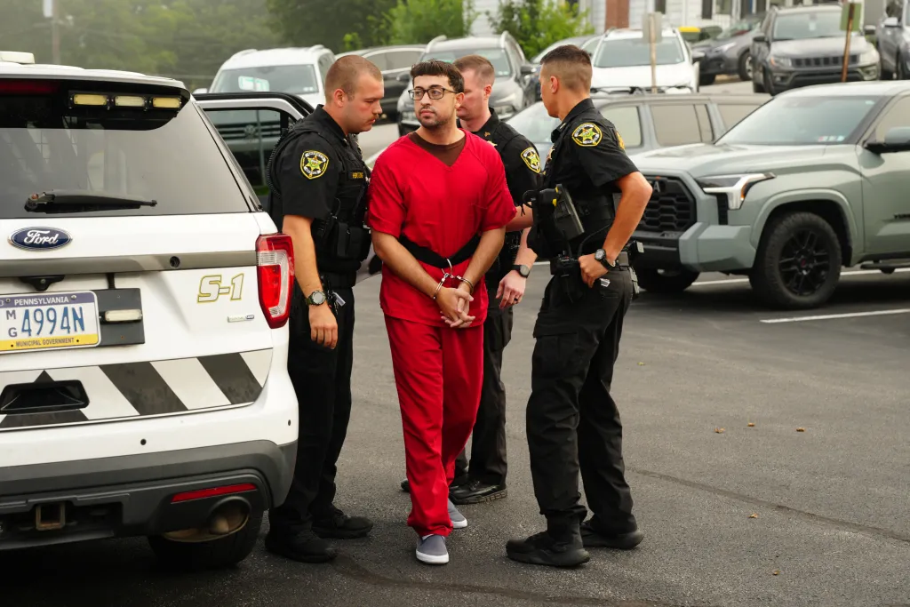 Agostino Abbatiello, in red, handcuffed and flanked by two police officers, outside a courthouse.