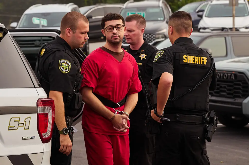 Agostino Abbatiello, 24, in red jumpsuit and handcuffs, escorted by three sheriff's deputies.