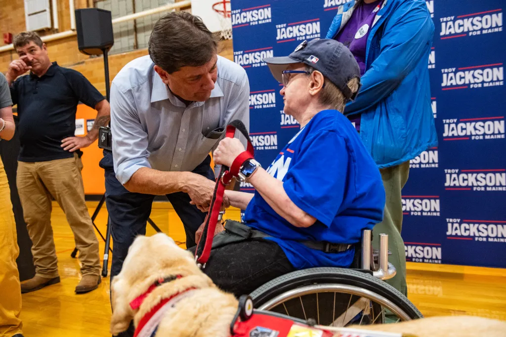 Troy Jackson talking to a woman in a wheelchair at a town hall event.