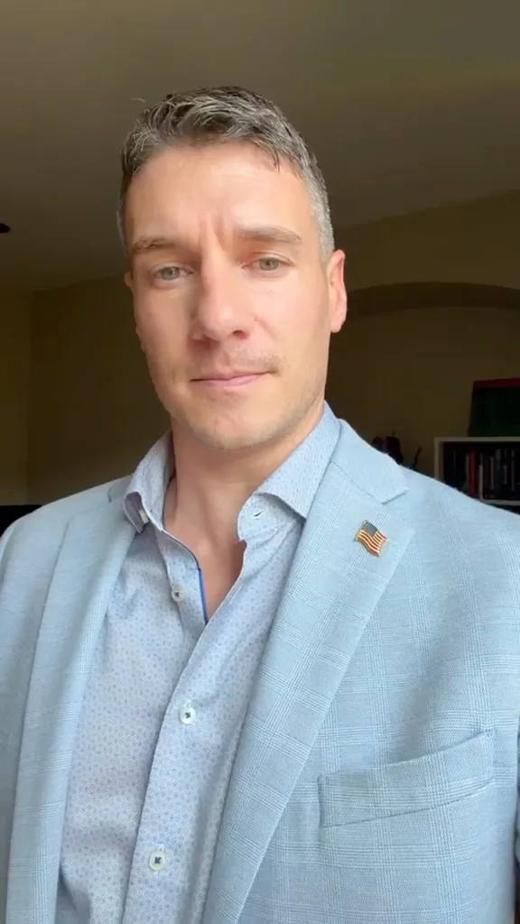 Chris Gallant wearing a light blue suit jacket with an American flag pin.