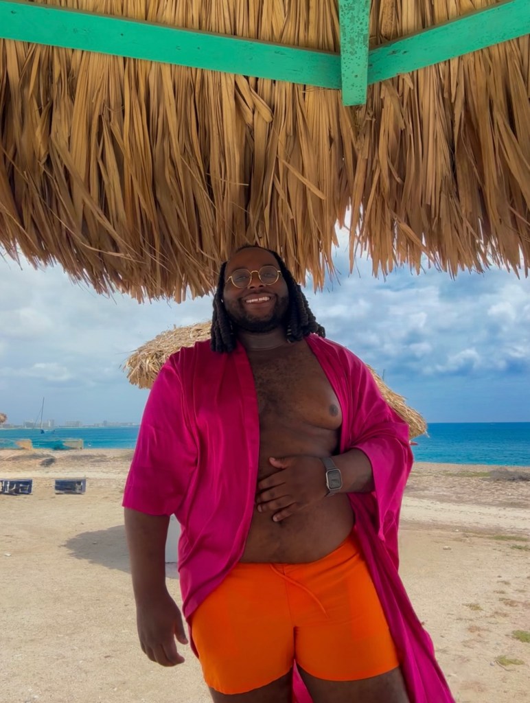 Da'Shaun L. Harrison smiling on a beach under a thatched roof.