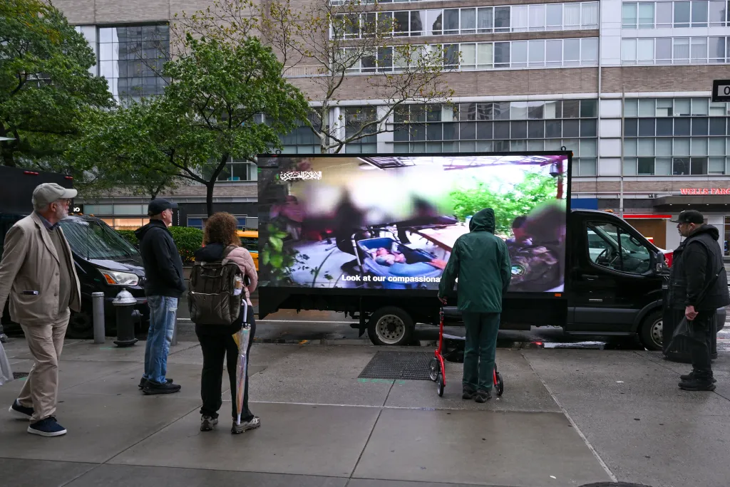 People gathered around a truck with a large video screen displaying footage of the October 7 Hamas attacks.