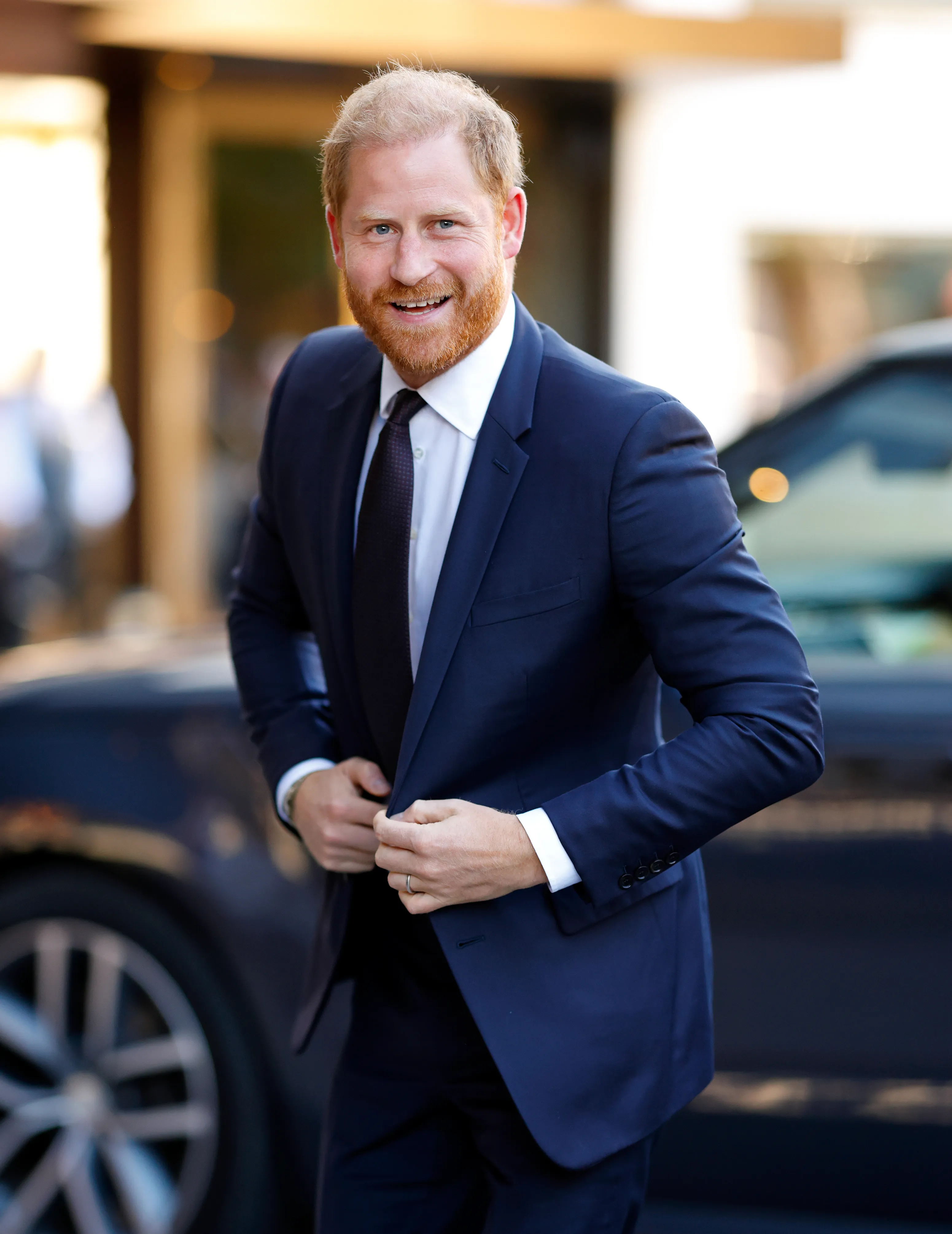 Prince Harry, Duke of Sussex, smiling and adjusting his suit jacket.
