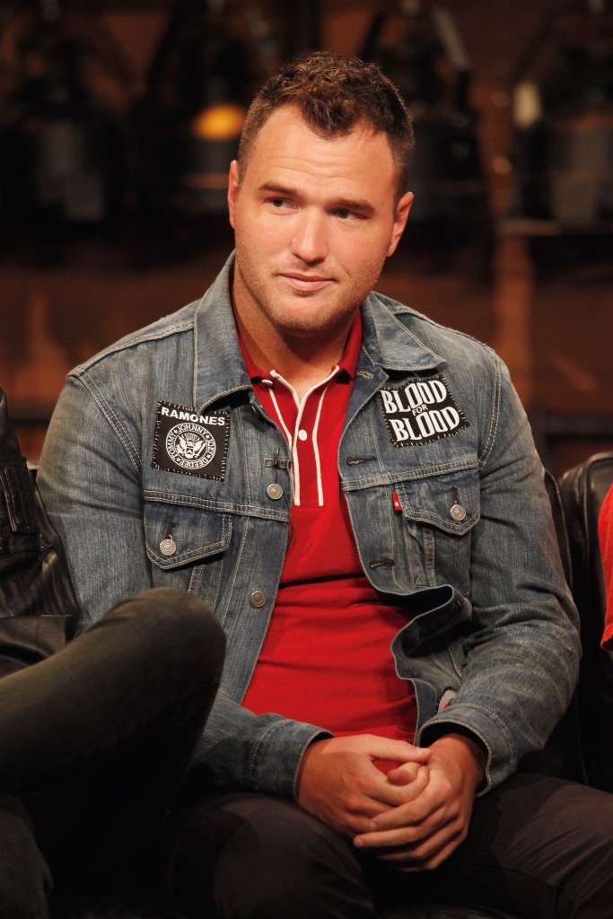 Chad Gilbert, guitarist of New Found Glory, in a denim jacket with patches over a red polo shirt, sits with clasped hands.