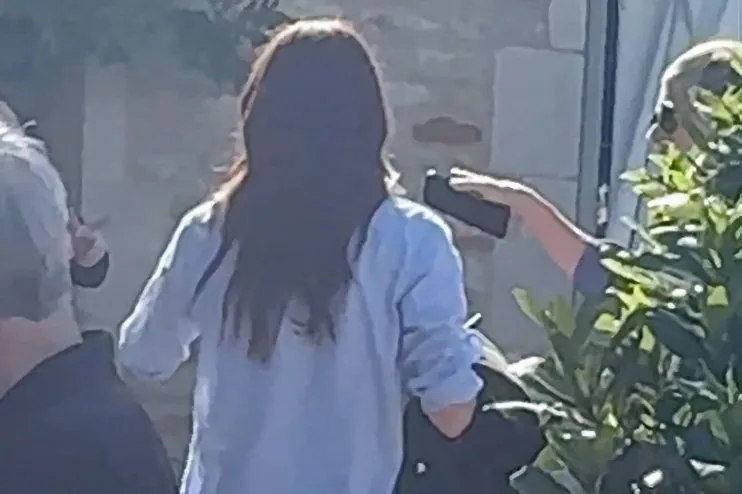 Meghan Markle seen from behind, walking away from Ellen DeGeneres who holds a phone.