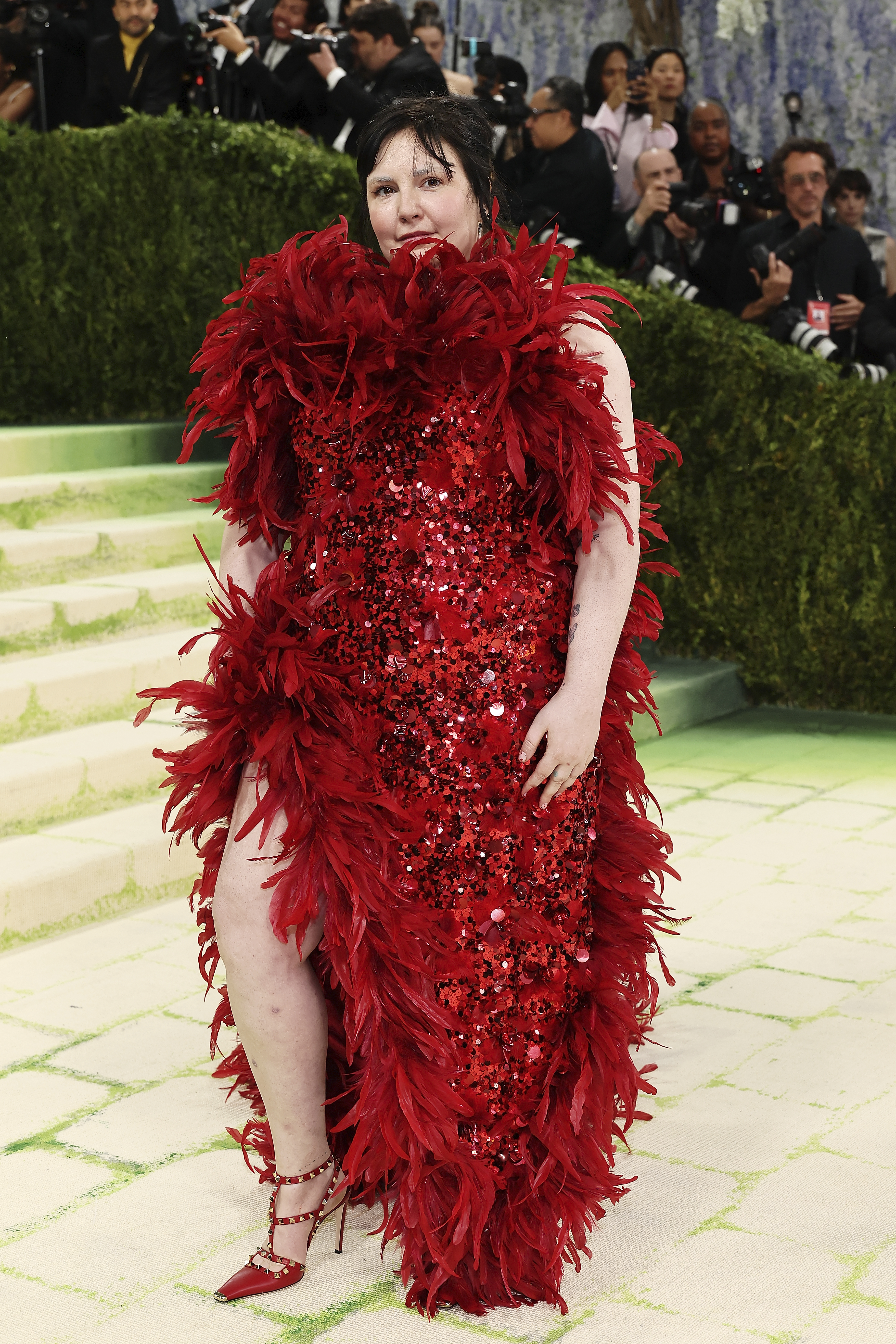 Lena Dunham wearing a red sequined dress with red feathers at the 2026 Met Gala.
