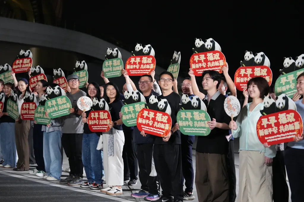 People hold up signs with pandas and Chinese characters to bid farewell to pandas Ping Ping and Fu Shuang.
