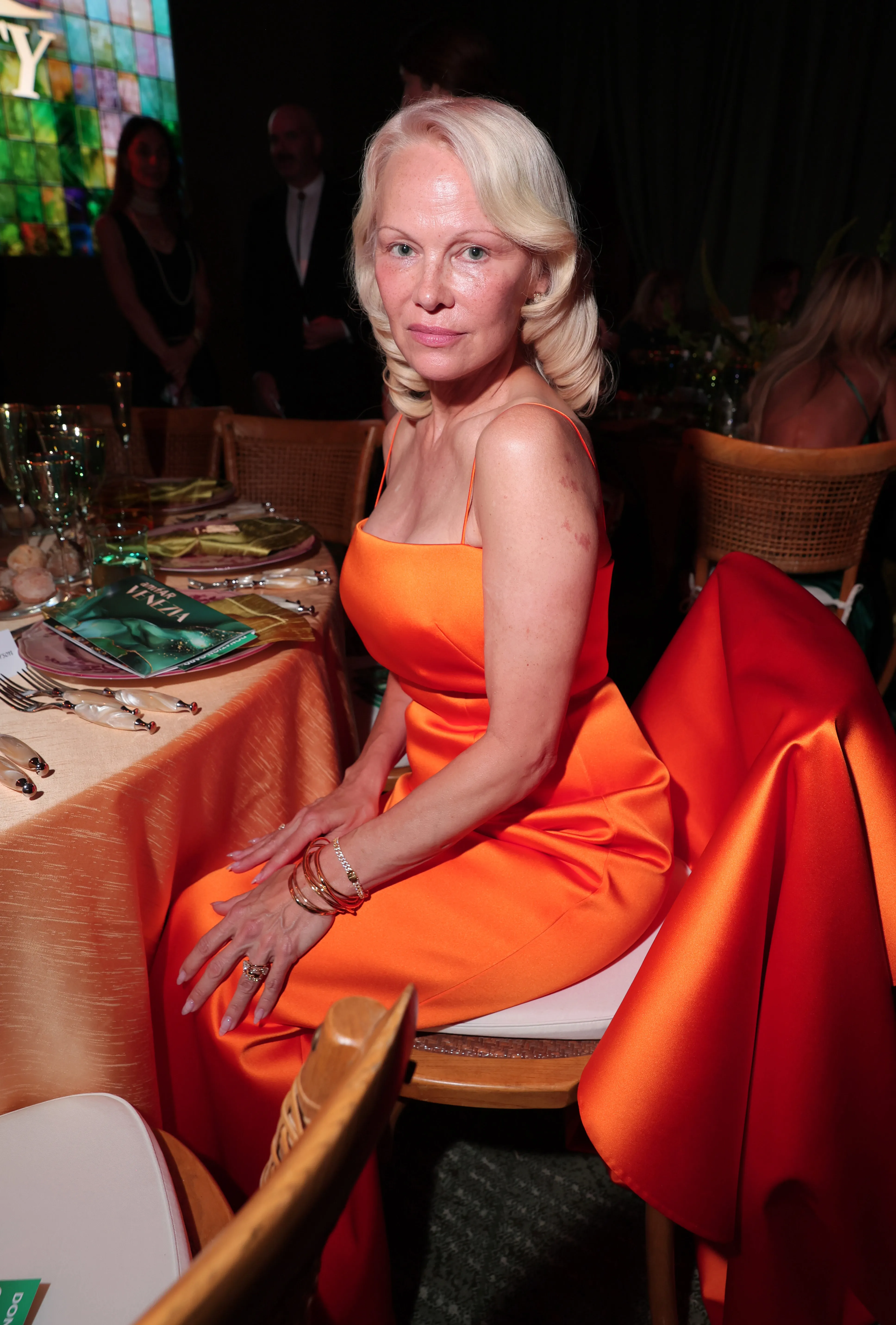 Pamela Anderson sits at a table during the amfAR Gala Venezia.