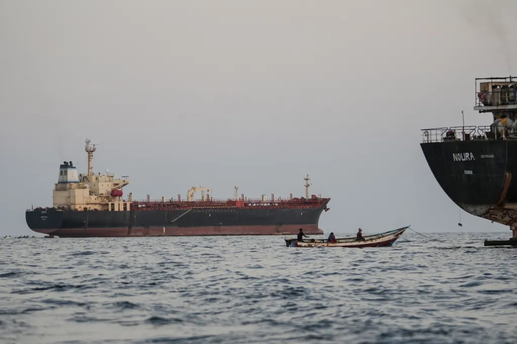 Commercial vessels anchored off Yemen's coast in the Bab al-Mandeb strait, with a small boat carrying three people in the foreground.