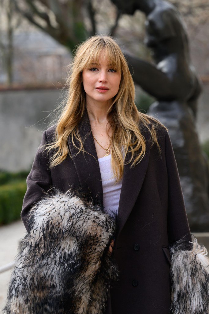 Jennifer Lawrence at Paris Fashion Week in a dark coat with a fluffy, shaggy lining and a gold necklace.