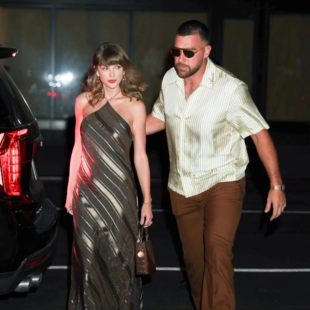 Taylor Swift wearing a metallic striped dress and Travis Kelce in a striped shirt, walking away from a car.