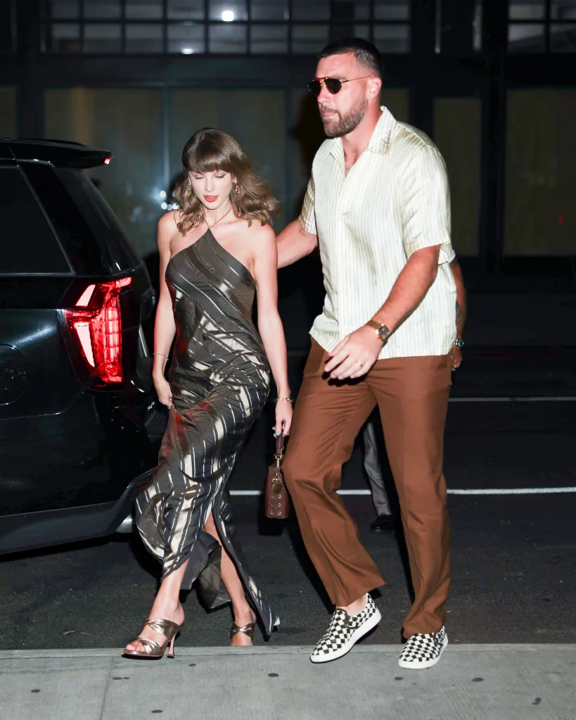 Taylor Swift in a metallic striped dress and Travis Kelce in a striped shirt, brown trousers, and checkered sneakers walking next to a black car.