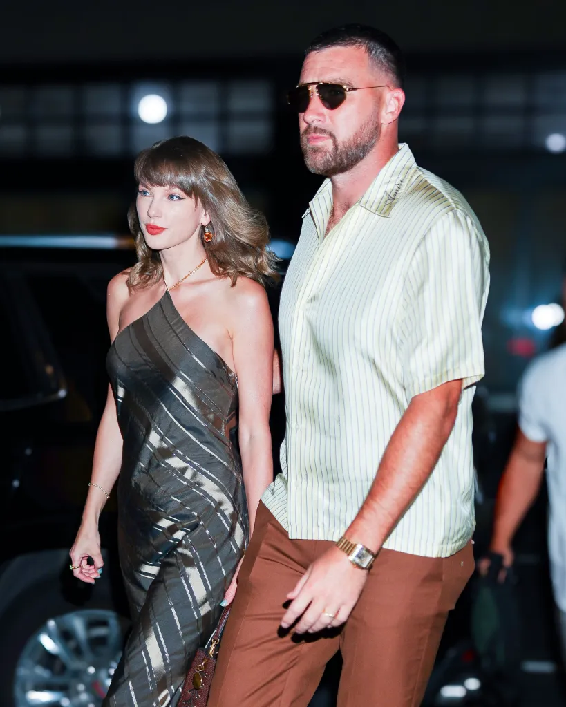 Taylor Swift in a metallic striped one-shoulder dress and Travis Kelce in a striped shirt and brown trousers walking side-by-side.