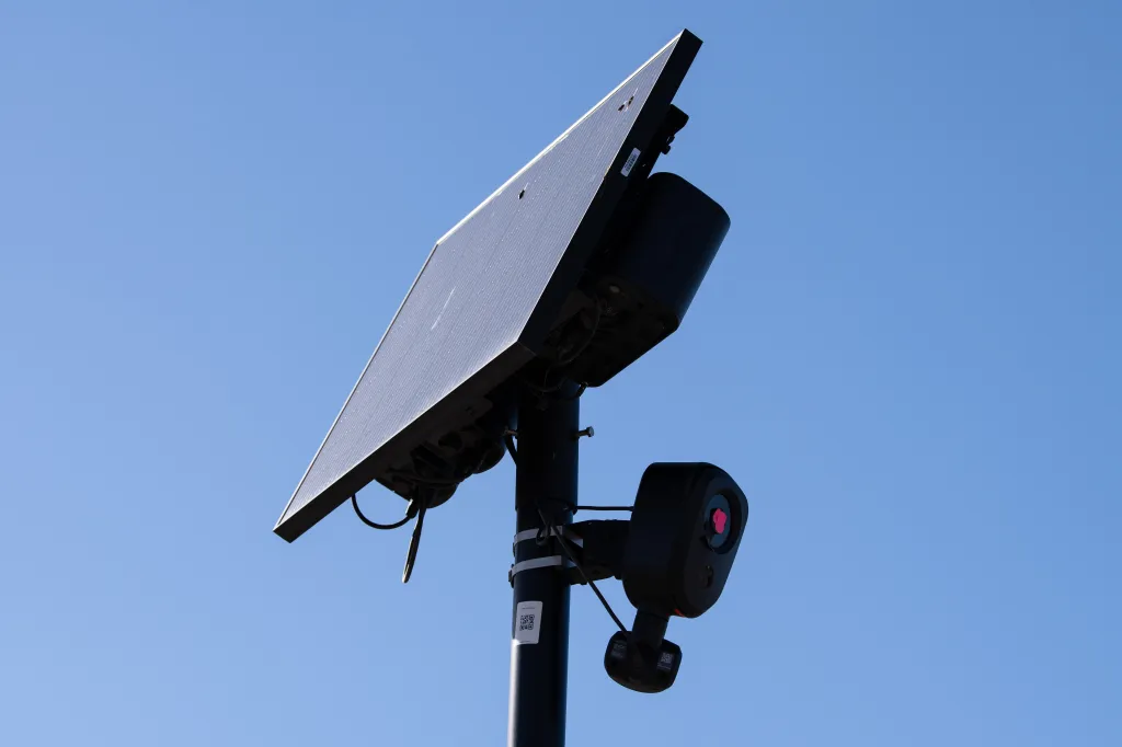 A solar-powered Flock Safety automated license plate reader (ALPR) camera against a clear blue sky.