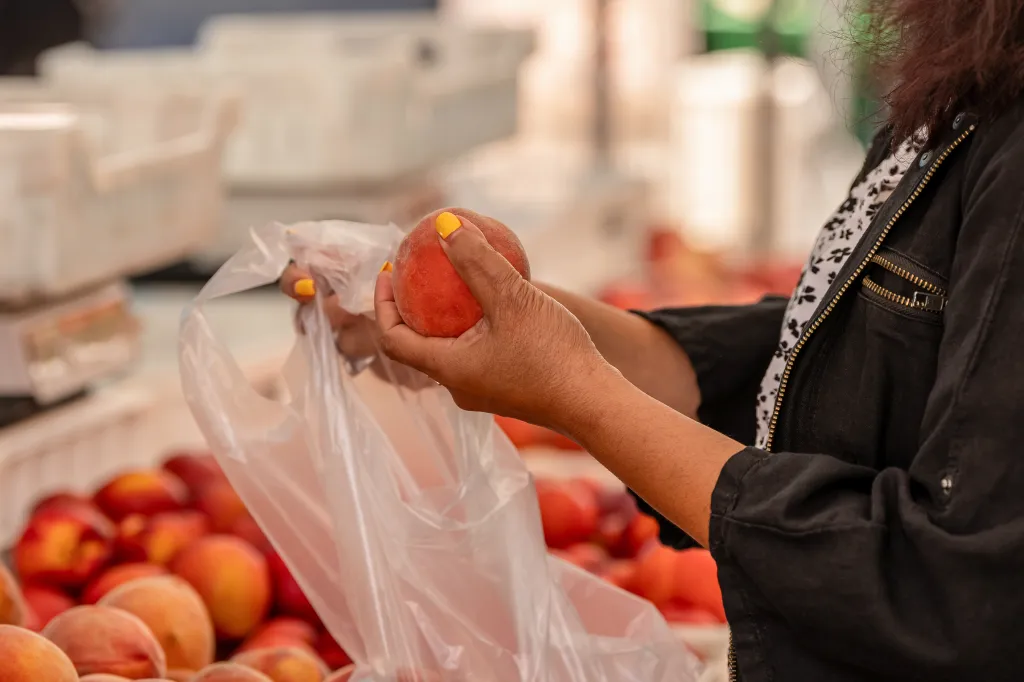 A shopper places a peach into a plastic bag at a farmers market.