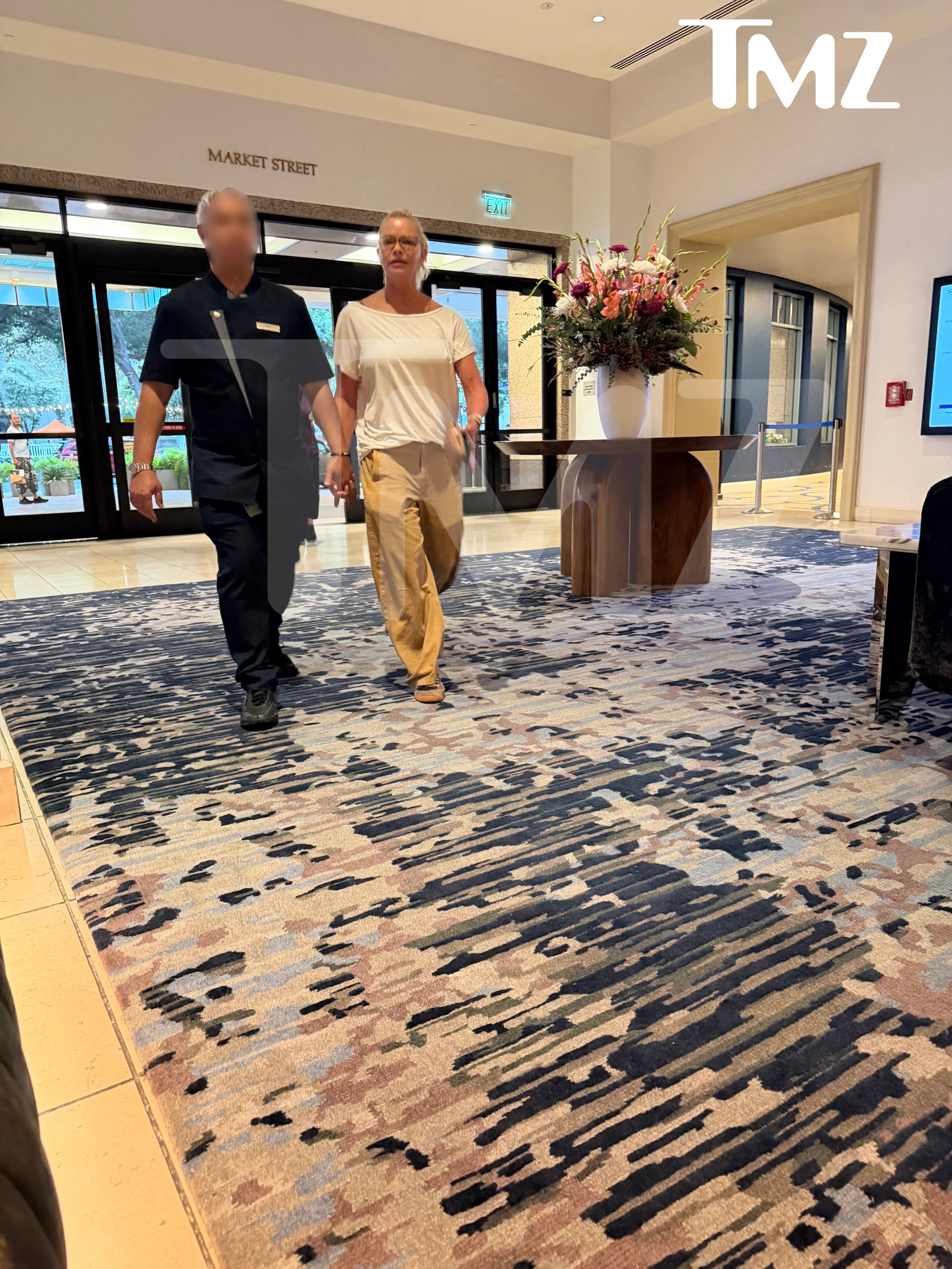 Jaime Pressly escorted by hotel staff, with a partially blurred face, walking out of a hotel lobby with a 