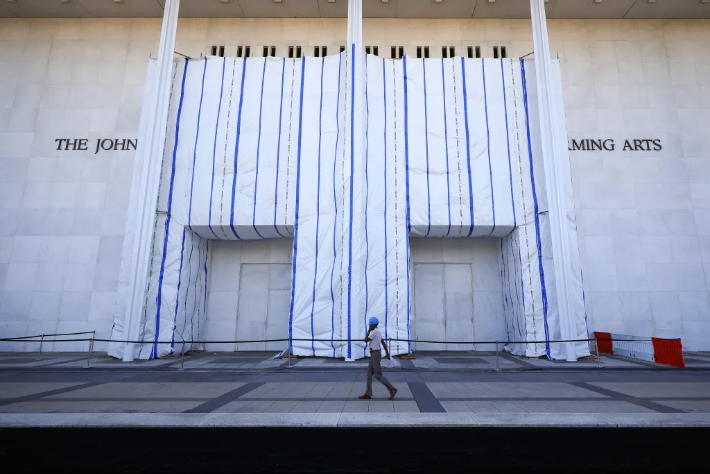 A worker walks past the Kennedy Center facade covered with white tarps with blue stripes.