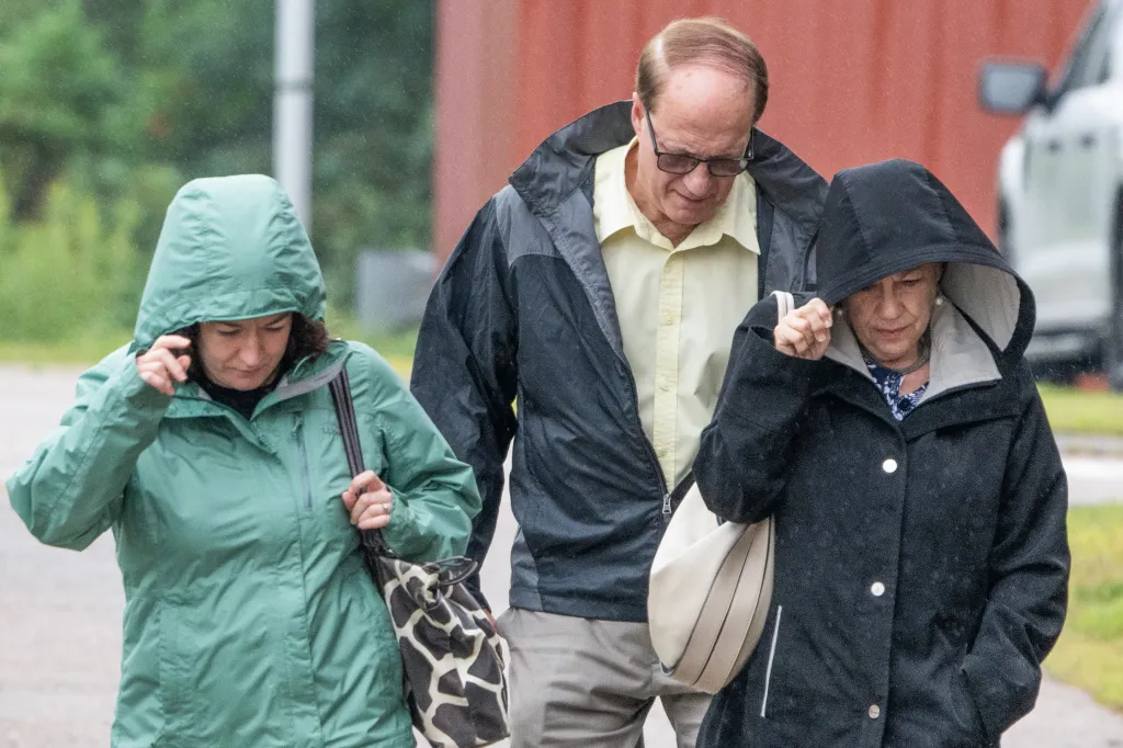 Three people walking outdoors in the rain.