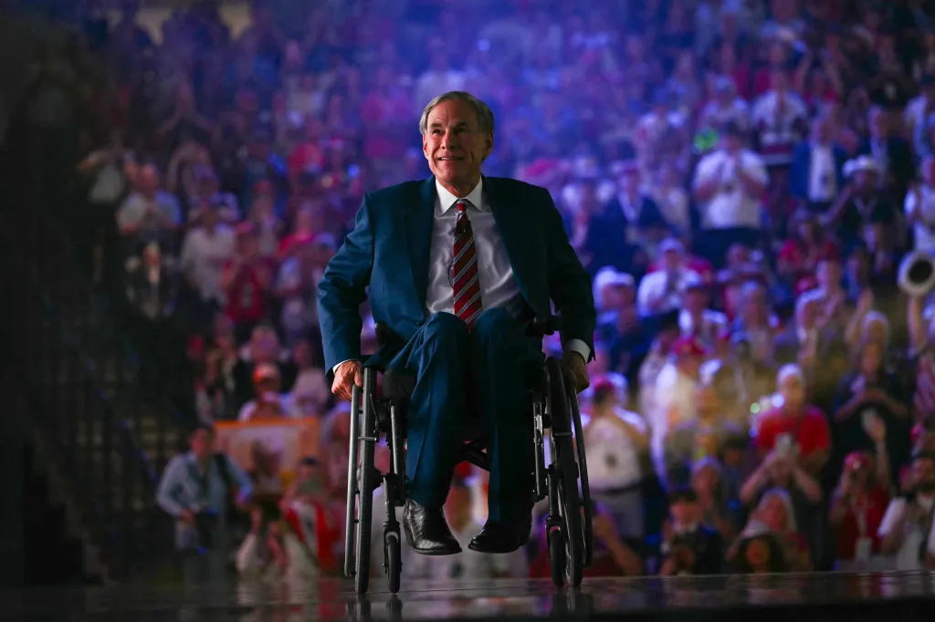 Governor Greg Abbott in a wheelchair smiling at a crowd.