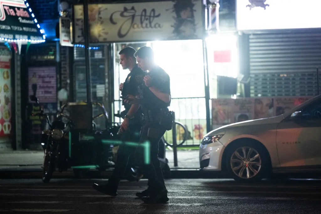 Two New York City Police Department officers patrol Roosevelt Avenue at night.