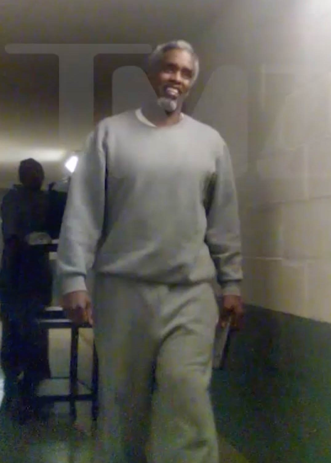 Sean Combs smiling while wearing a gray prison uniform at Fort Dix.