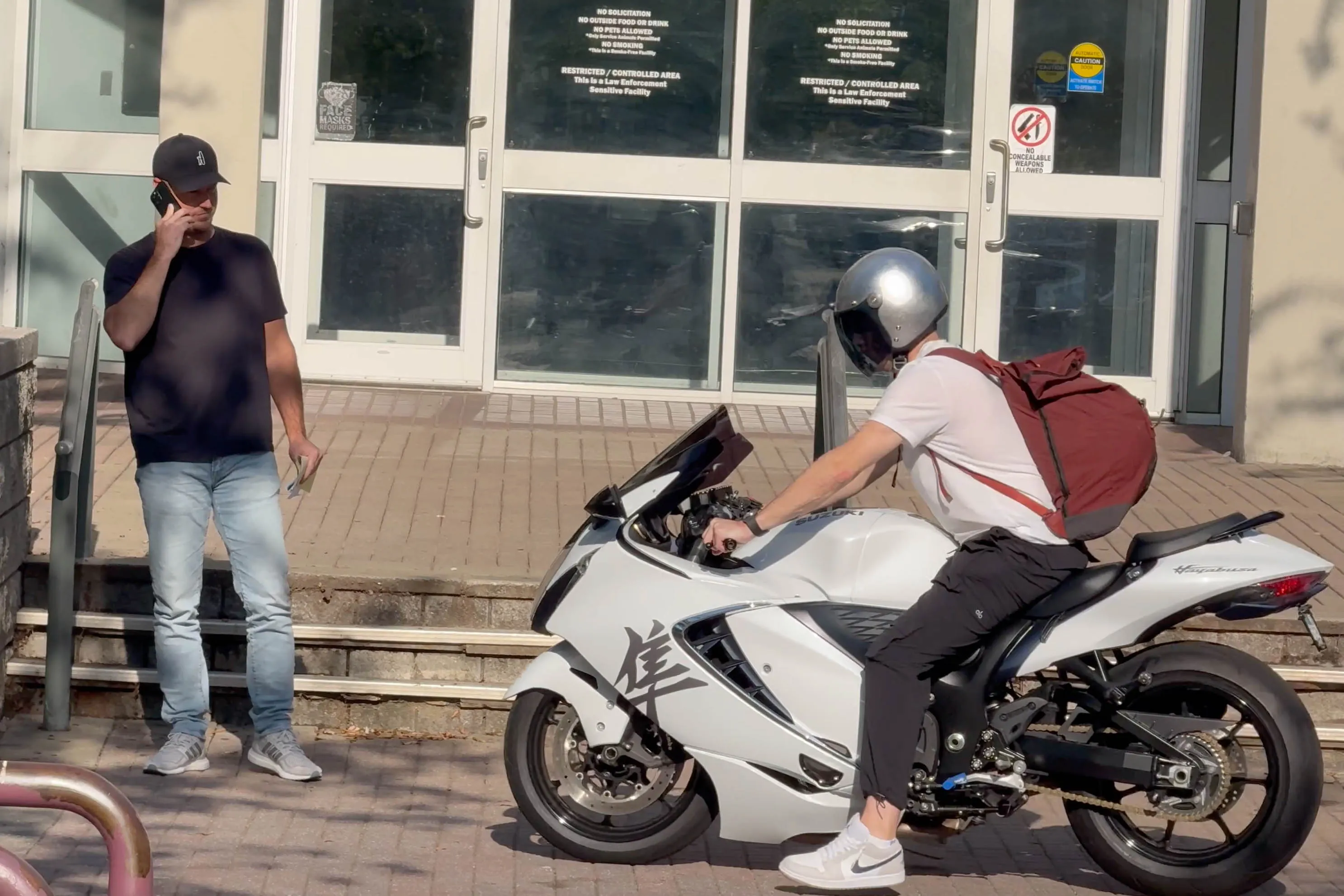 Zach Hickerson talking on the phone after leaving jail in Greenville, with another person on a white motorcycle beside him.