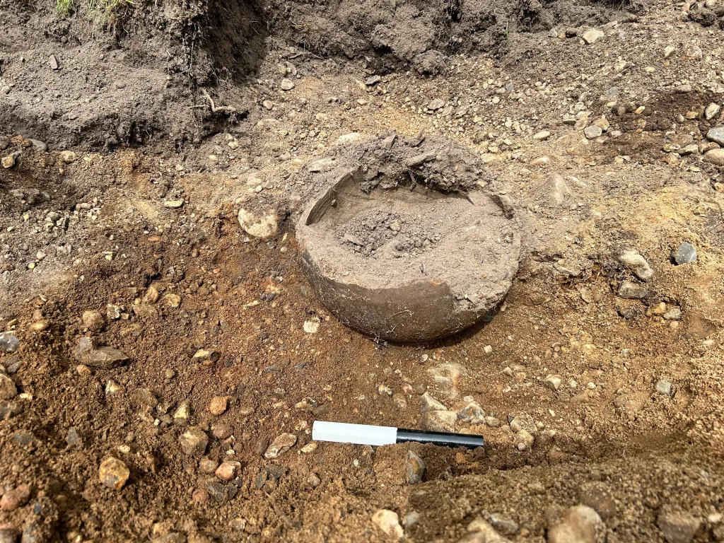An ancient clay vessel, unearthed in the ground, still filled with soil.