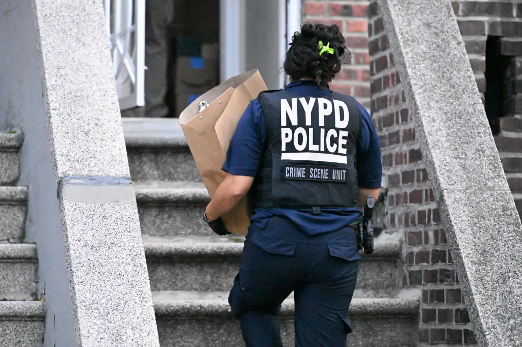 NYPD Crime Scene Unit officer carrying a brown evidence bag walks up stone stairs.
