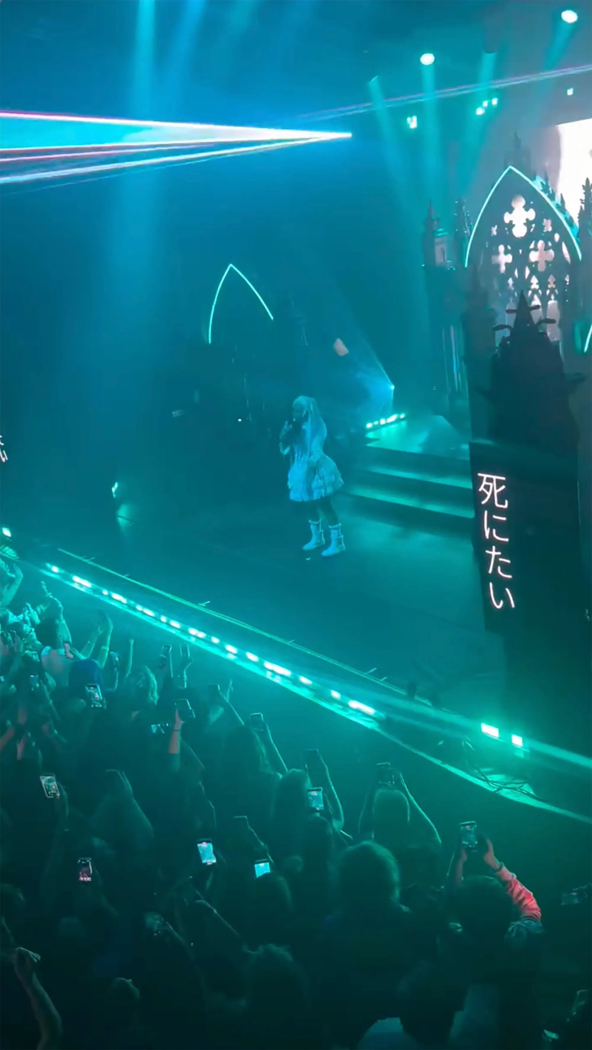 North West performing on stage at her first solo concert, illuminated by blue stage lights.
